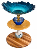 The Maylan tiered serving tray with teal sunburst glass top bowl, cobalt blue flower accent, mustard yellow ceramic plate, glazed ceramic stem, and striped wood base